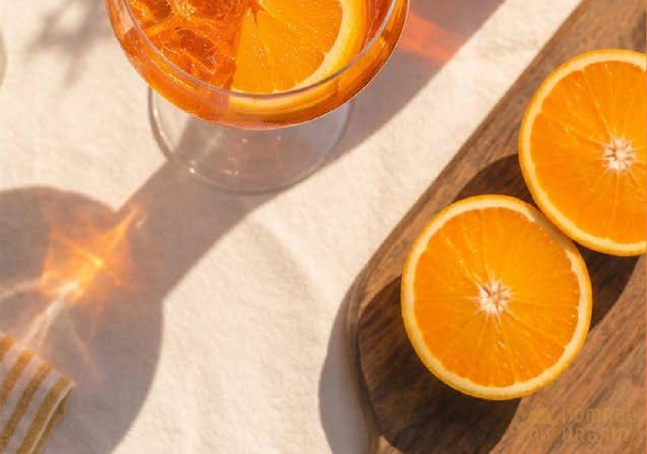 Verre d'ABK6 Orange Spritz à côté d'oranges coupées en deux sur une planche en bois