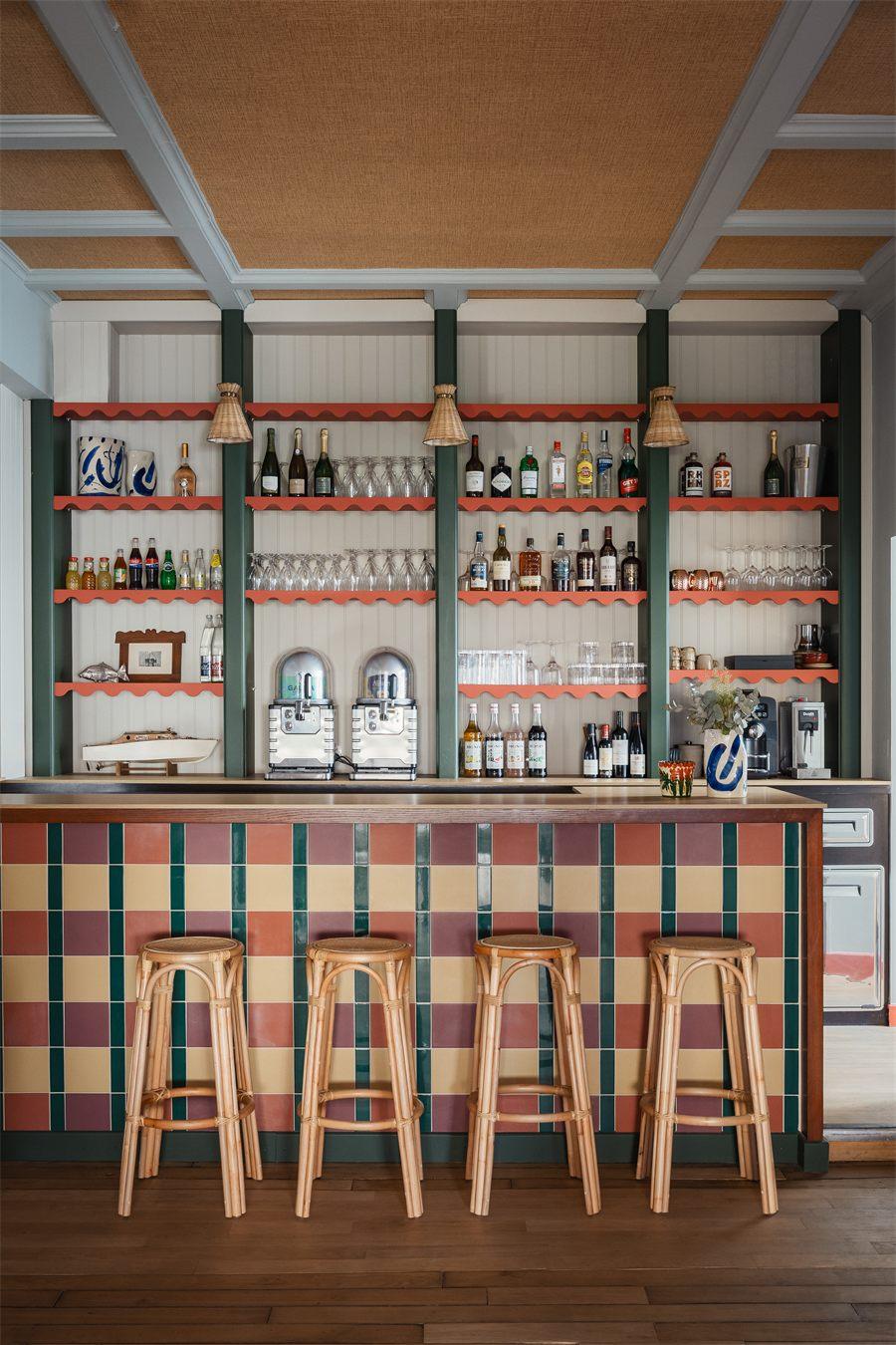 Comptoir du bar en faïence à damier vert, rose et jaune, tabourets en rotin
