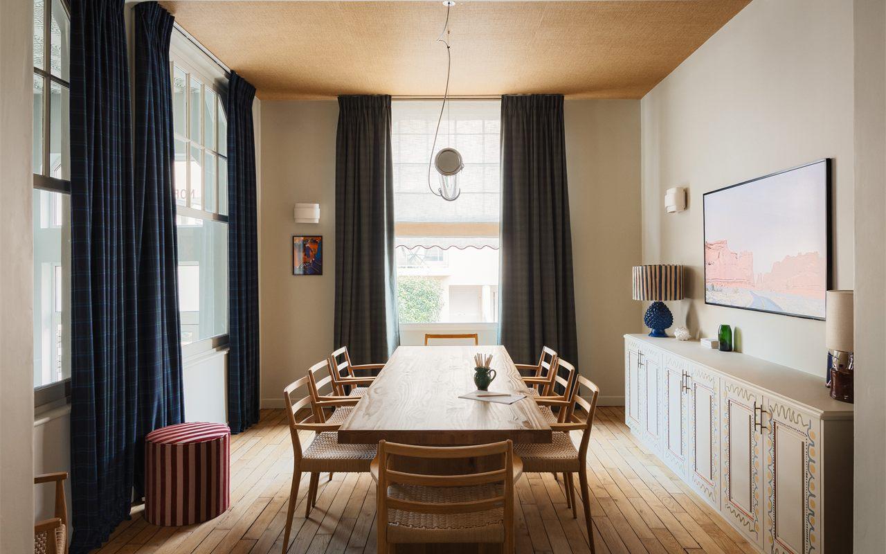 Salle à manger avec grande table en bois, buffet peint à motifs et rideaux tartan