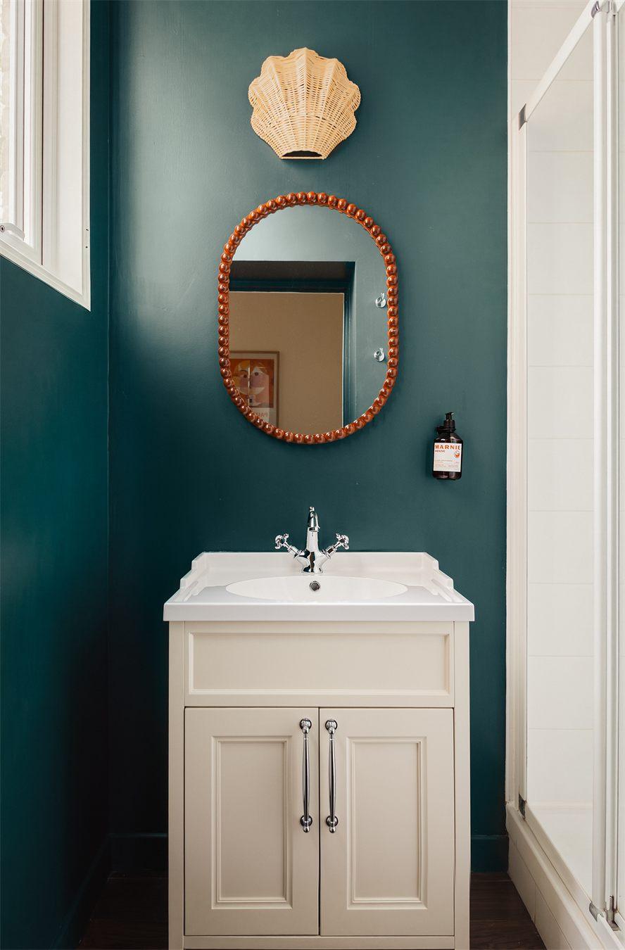 Salle de bains vert canard avec miroir à perles et applique en rotin en forme de coquillage