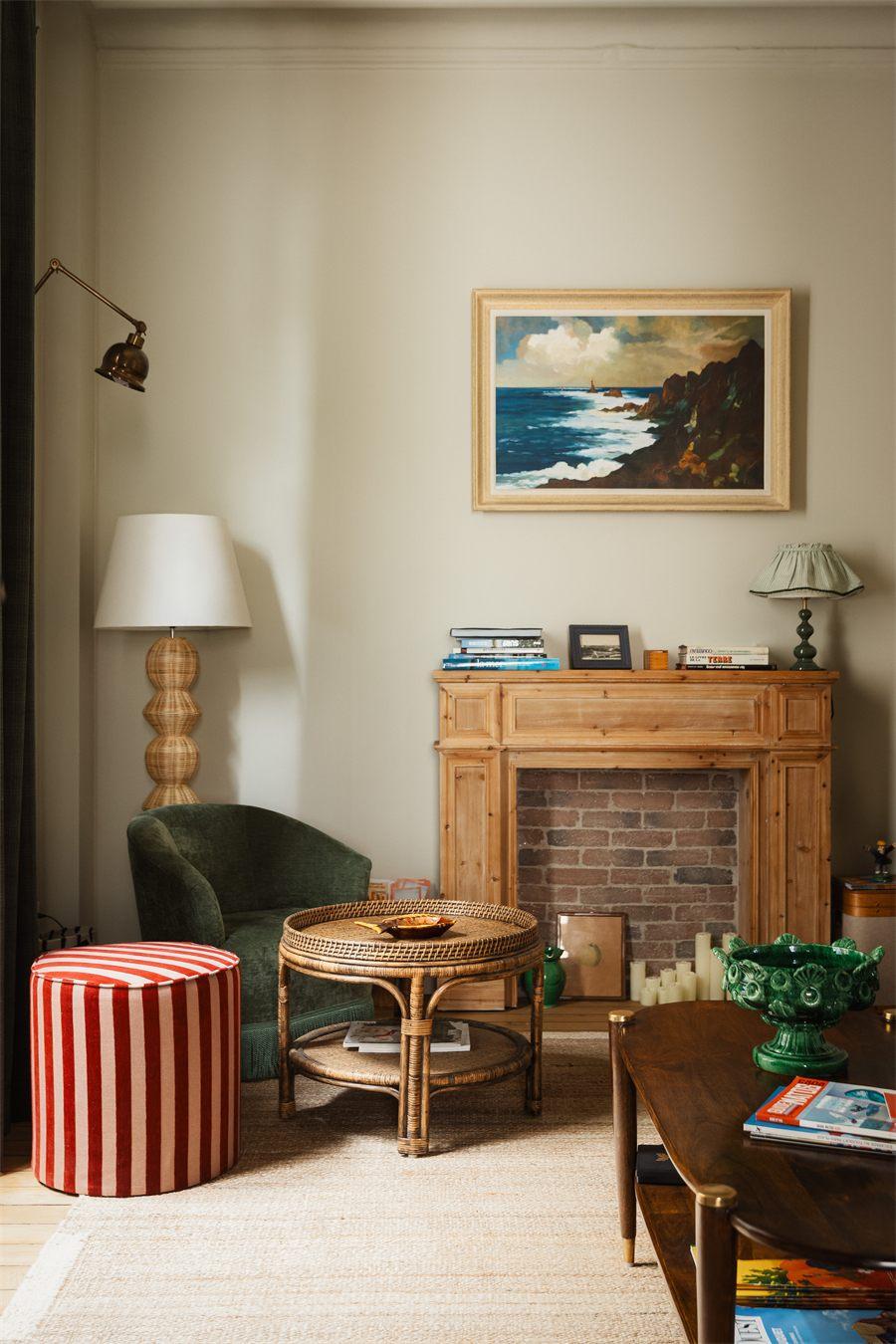 Salon de Marnie House avec cheminée de bois, fauteuil vert et pouf rayé rouge