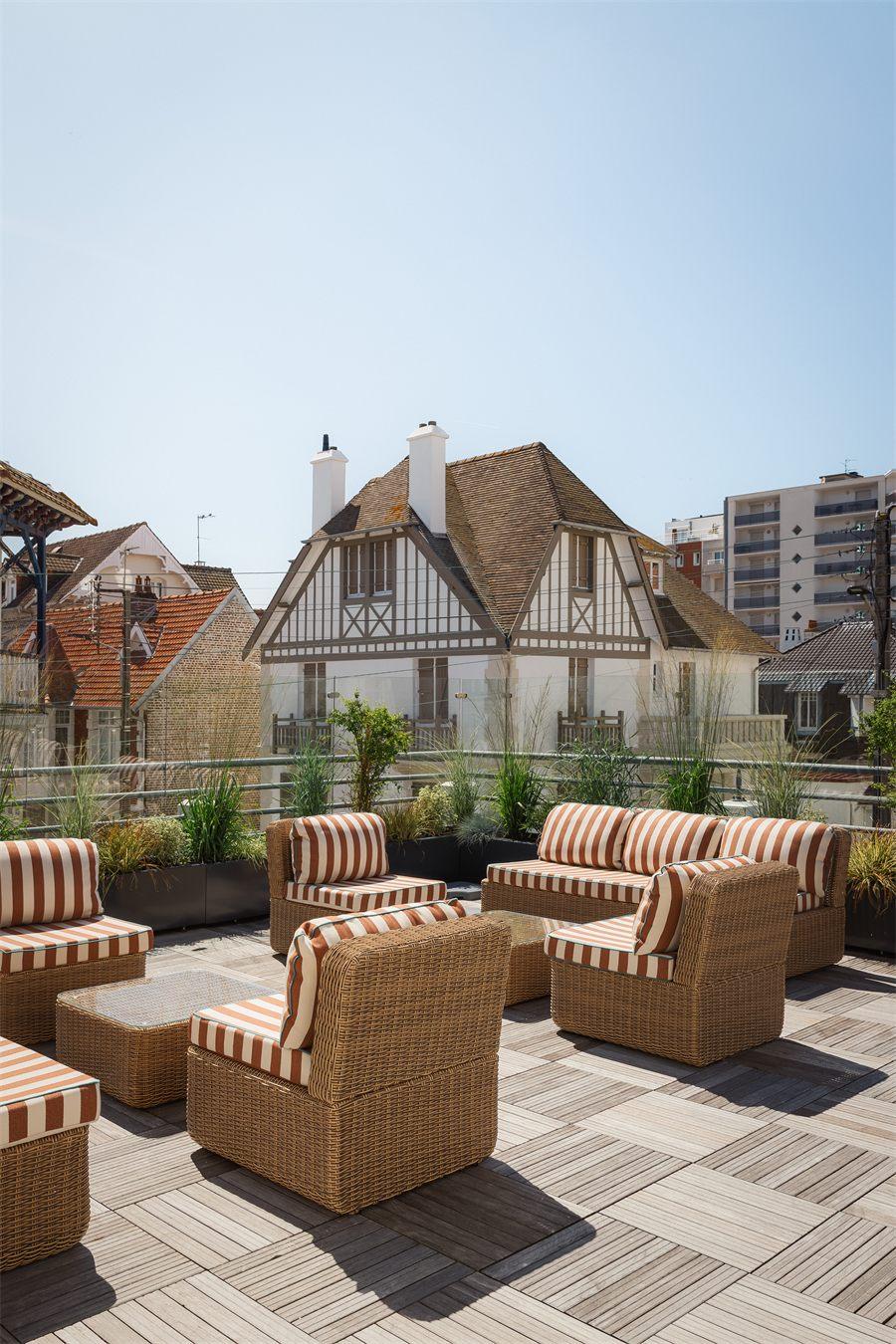 Terrasse en teck sur le toit, fauteuils en rotin à rayures orangées face aux colombages