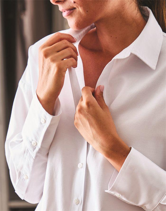 Une femme ajuste le col de sa chemise blanche defroissee