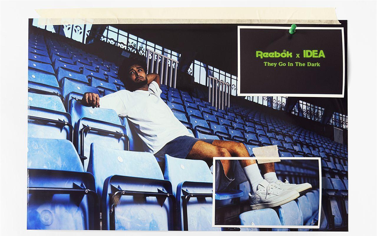 Homme allonge dans des gradins bleus, chausse de la Reebok x IDEA Club C 85