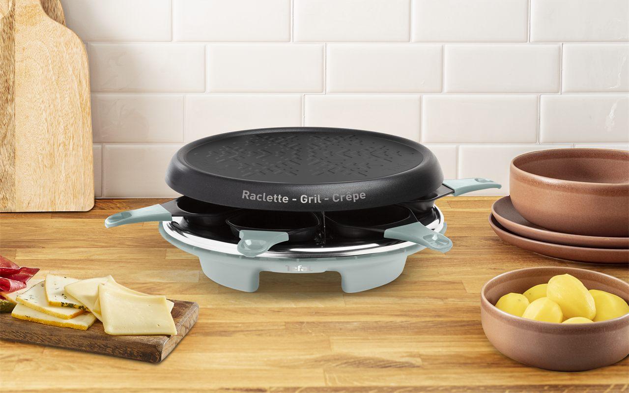 L'appareil à raclette Tefal posé sur un plan de travail en bois, entre une planche de fromage et un bol de pommes de terre