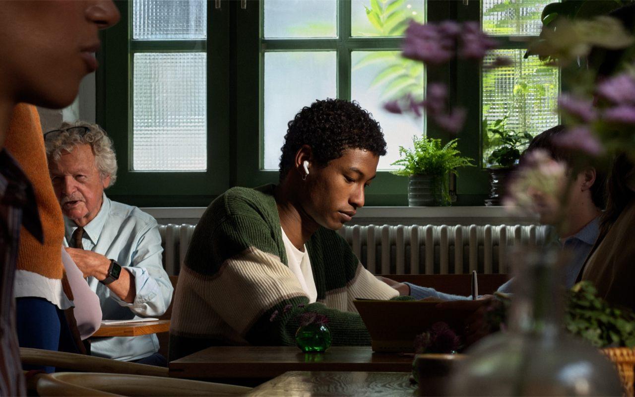 Un homme travaille dans un café animé, un écouteur AirPods 5 à l'oreille