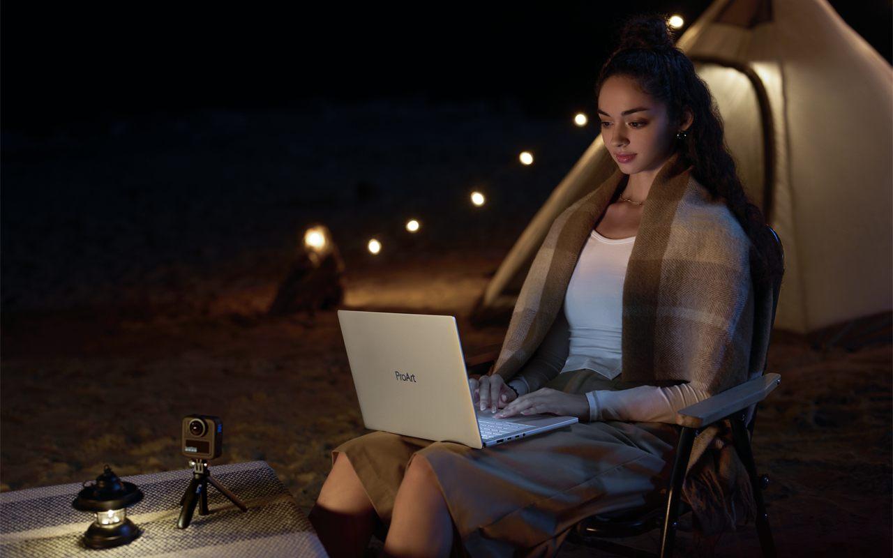 Une créatrice travaille sur son ASUS ProArt P14 le soir, sous un auvent éclairé de guirlandes