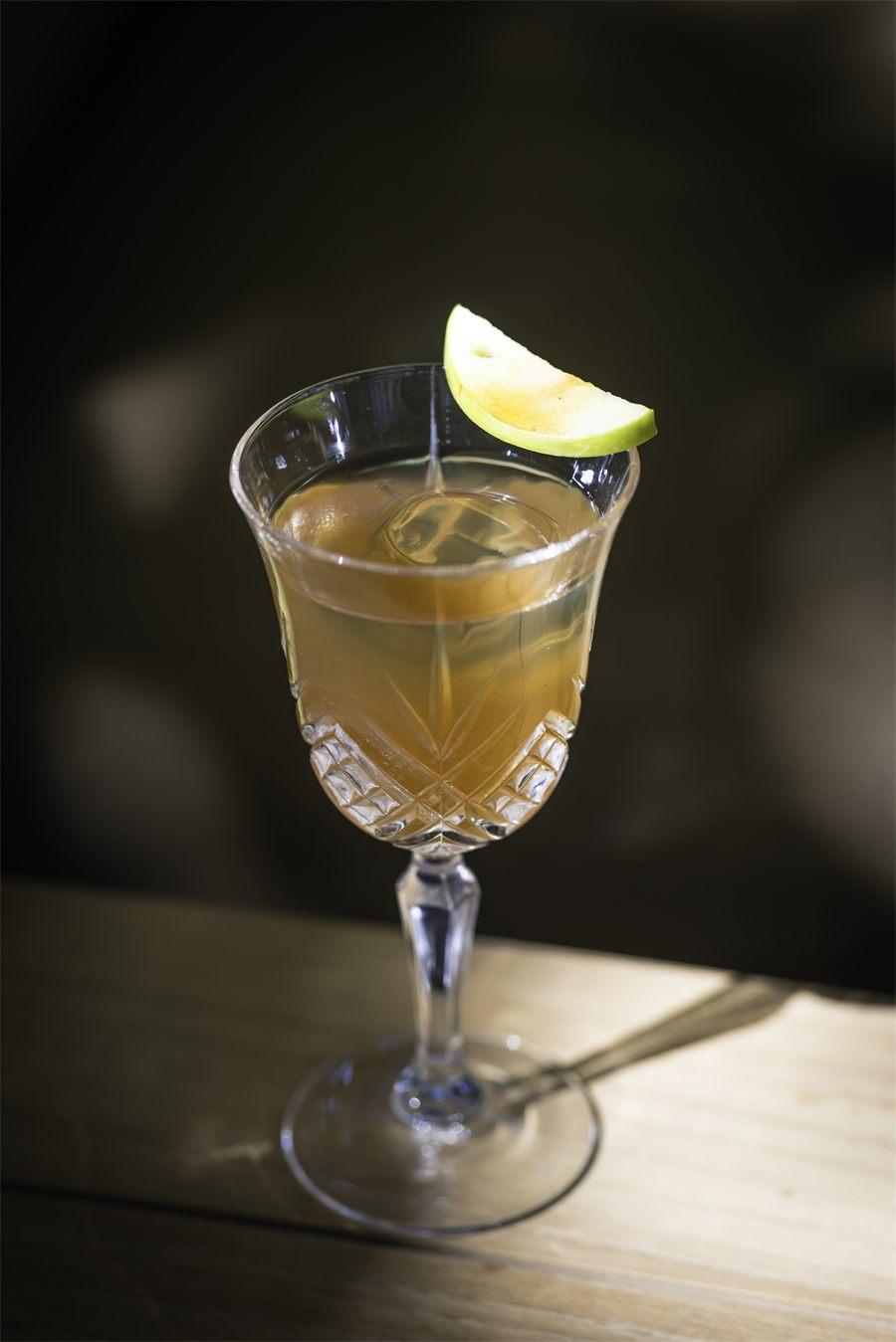 Verre taillé, cocktail ambré et quartier de pomme verte sur le bord