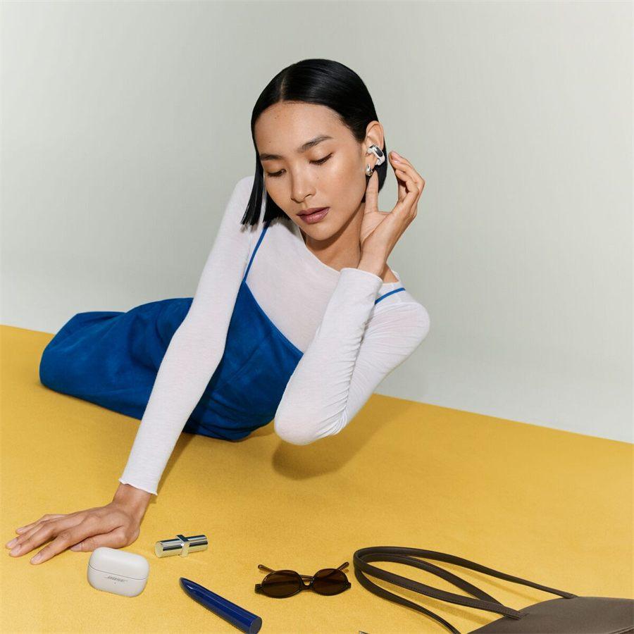 femme allongée sur fond jaune, étui des Bose Ultra Open Earbuds posé à côté d'elle
