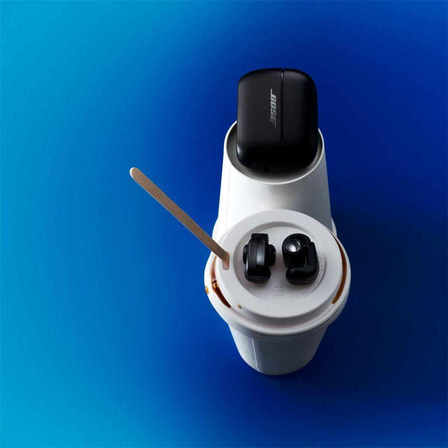 étui noir des Bose Ultra Open Earbuds en équilibre sur un gobelet de café