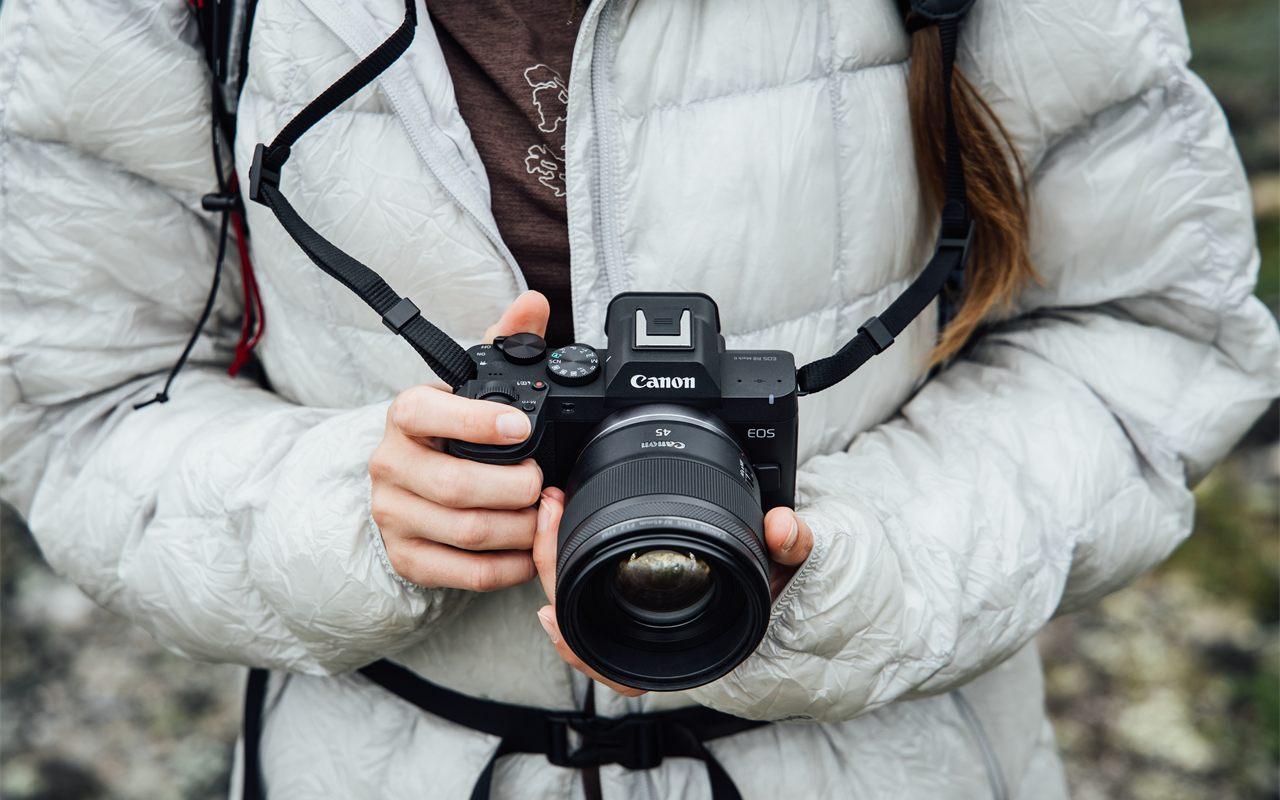 Mains tenant le Canon EOS R8 Mark II a main levee en exterieur