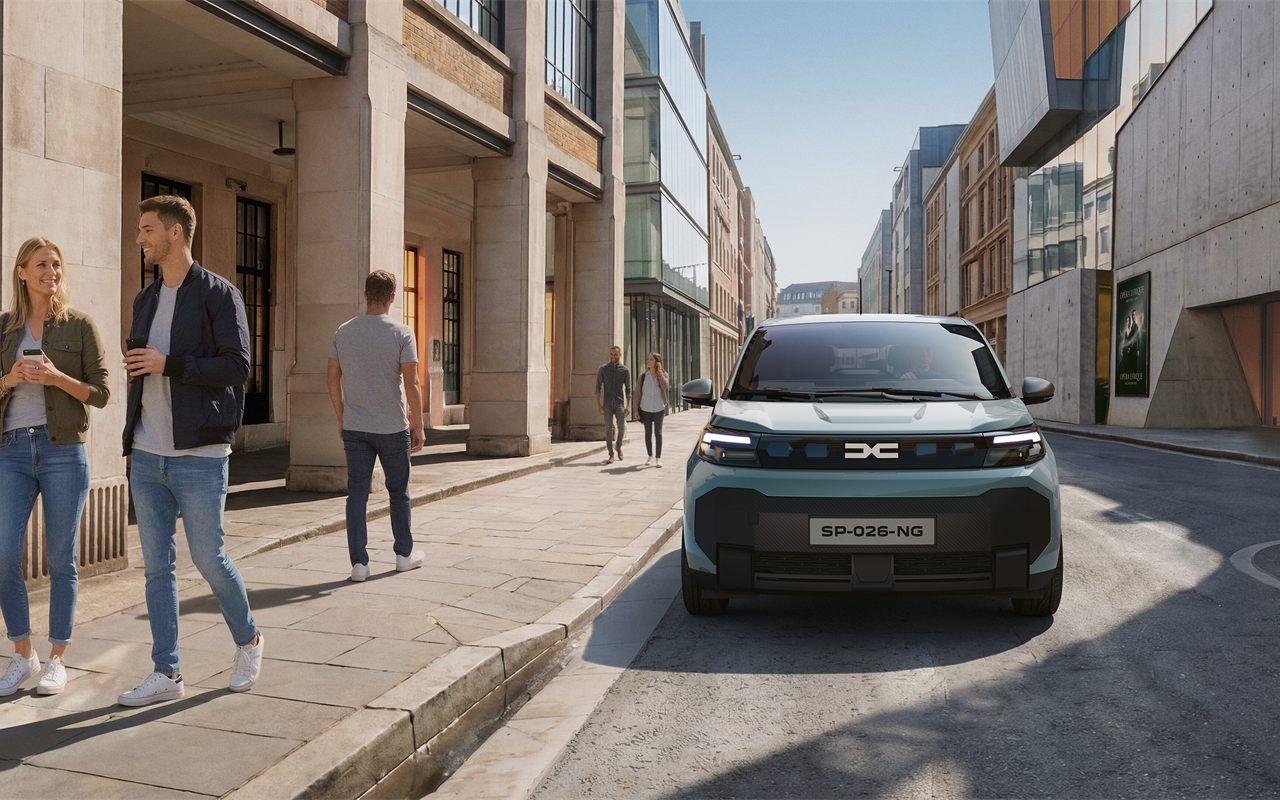 Face avant de la Dacia Spring à l'arrêt dans une rue, deux passants au premier plan