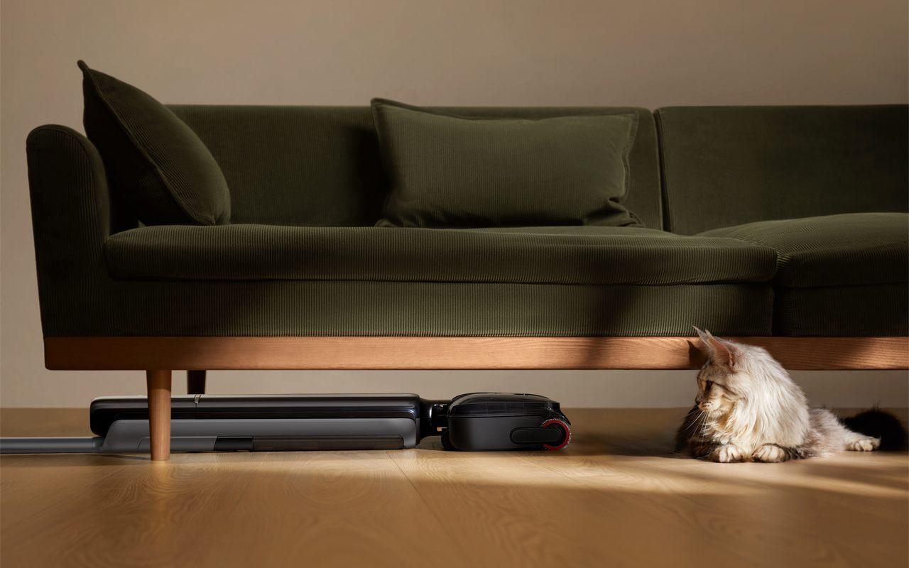 Aspirateur balai laveur Dreame T Series couché à plat sous un canapé en velours vert