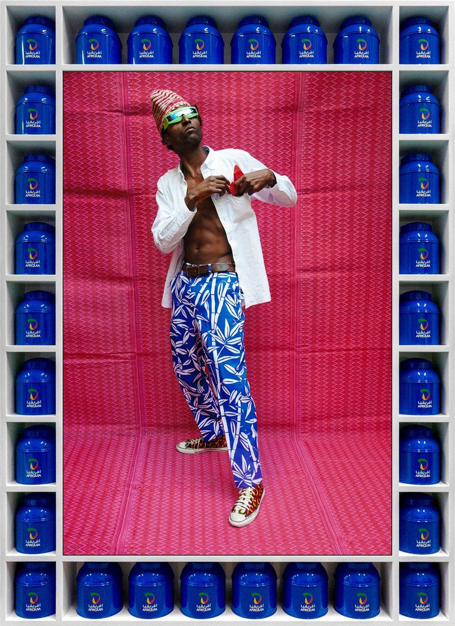 Keziah Jones en chemise blanche, cadre en bidons d'huile bleus