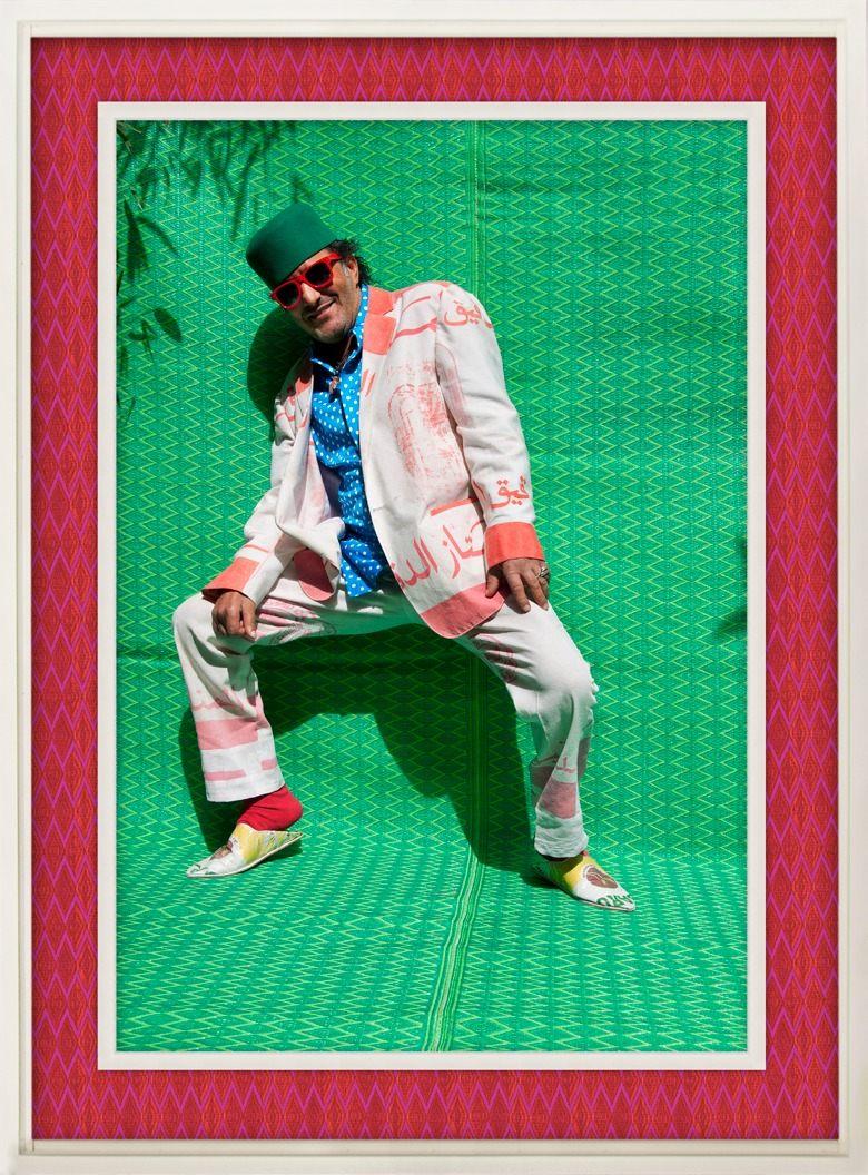 Rachid Taha en costume blanc et rose devant une natte verte