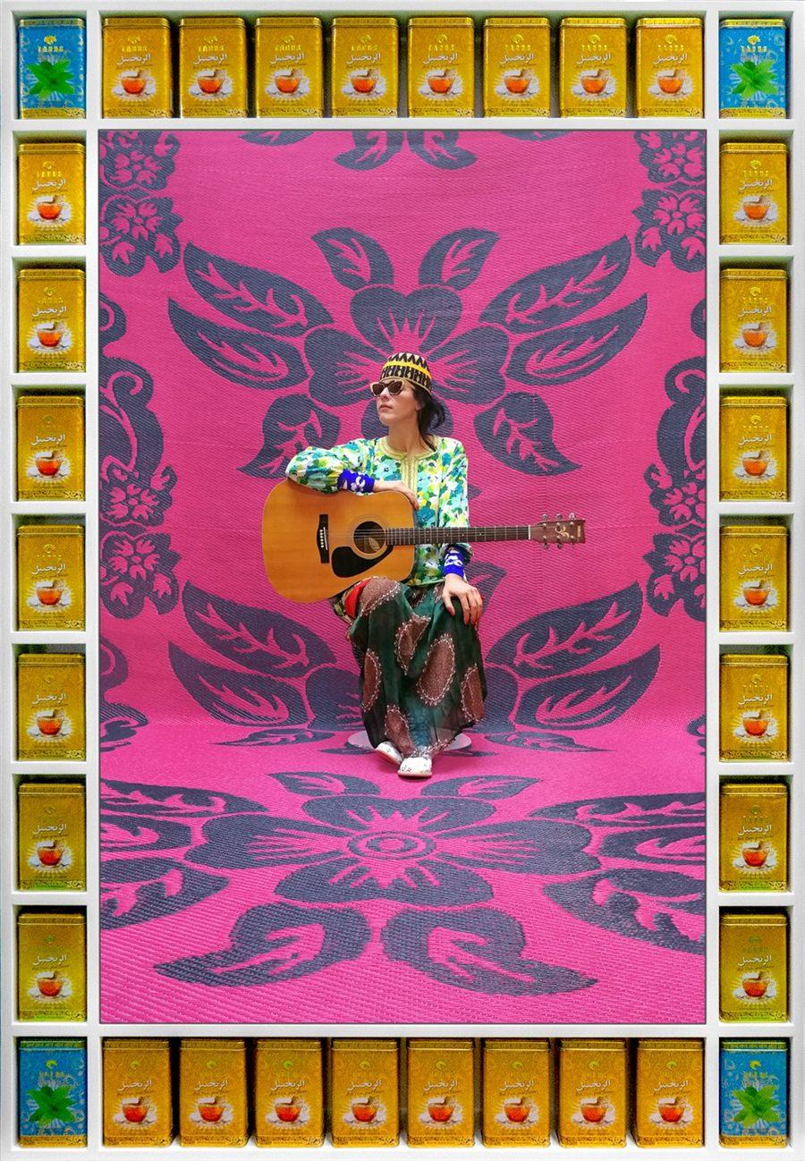 Souad Massi et sa guitare devant une natte rose à fleurs, cadre en boîtes de thé