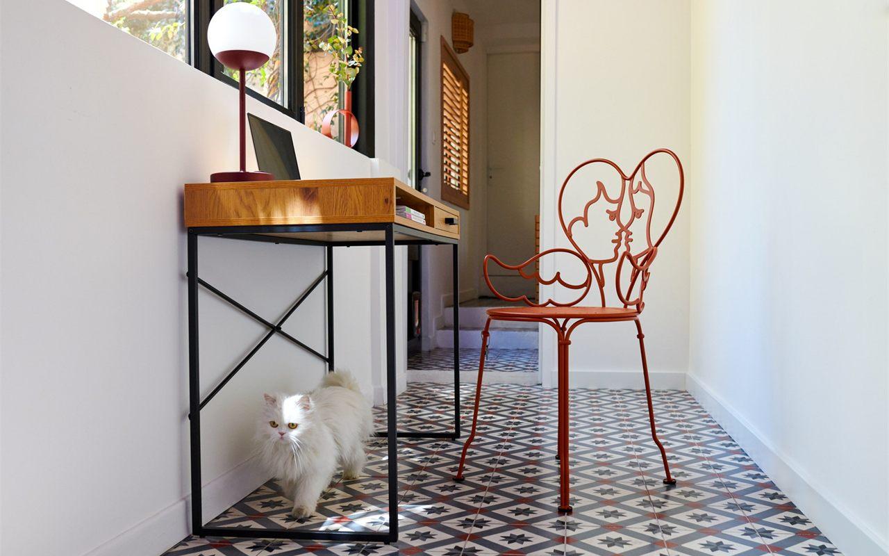 La chaise Ange de Castelbajac pour Fermob, en ocre rouge, dans un couloir aux carreaux de ciment