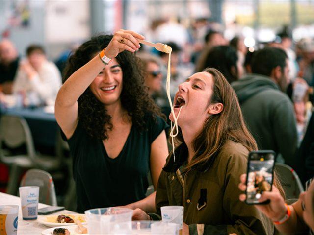 Une convive tend un fil d'aligot au-dessus de la table pendant l'Aligofest