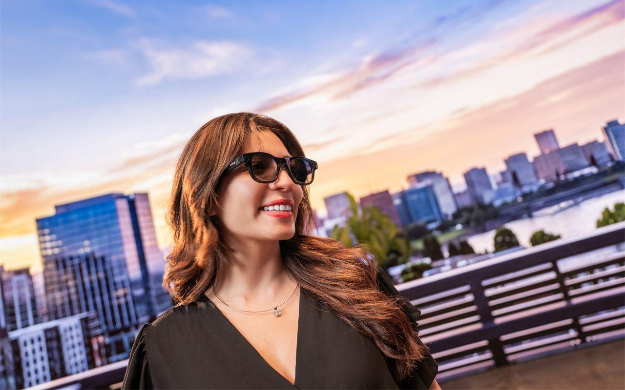 Une femme porte les lunettes connectées HTC VIVE Eagle devant une skyline au coucher du soleil