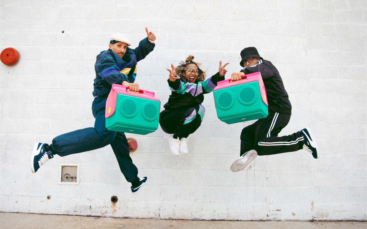 Trois danseurs sautent devant un mur blanc, deux glacières Igloo KoolTunes à la main