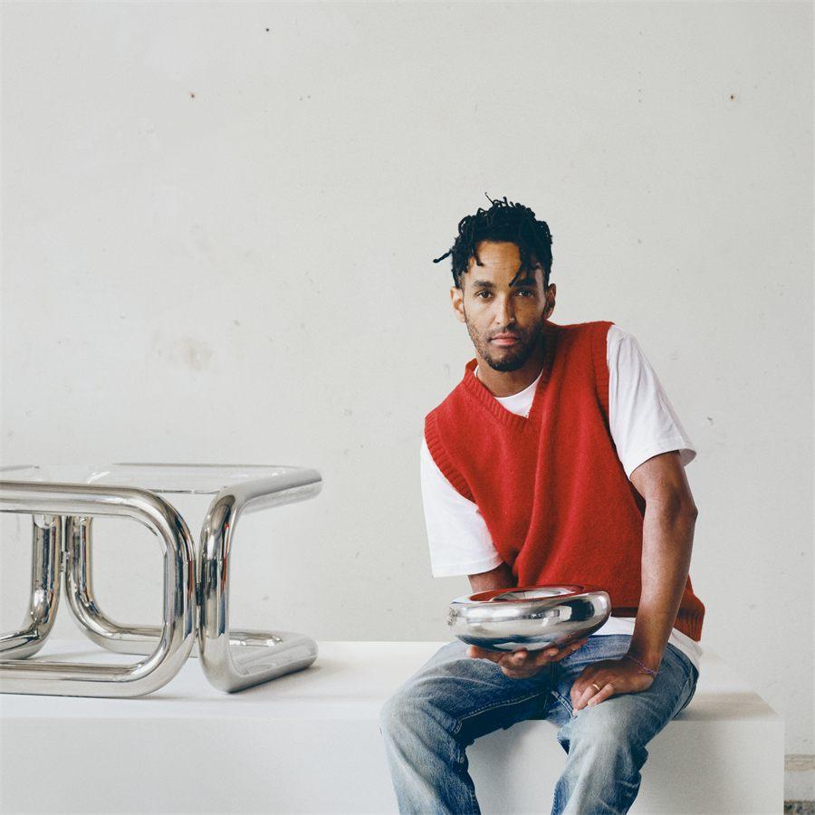 Le designer Andu Masebo assis près de sa table d'appoint chromée KONSTRUNDA