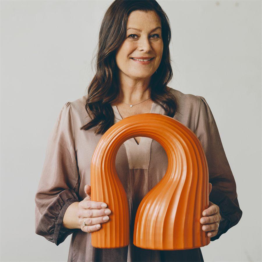 La designer Lisa Hilland tenant son arche décorative orange KONSTRUNDA