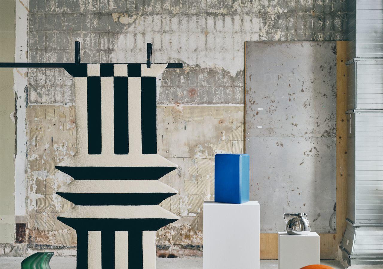 Tapis noir et blanc suspendu au mur, arche orange et vase vert de la collection KONSTRUNDA