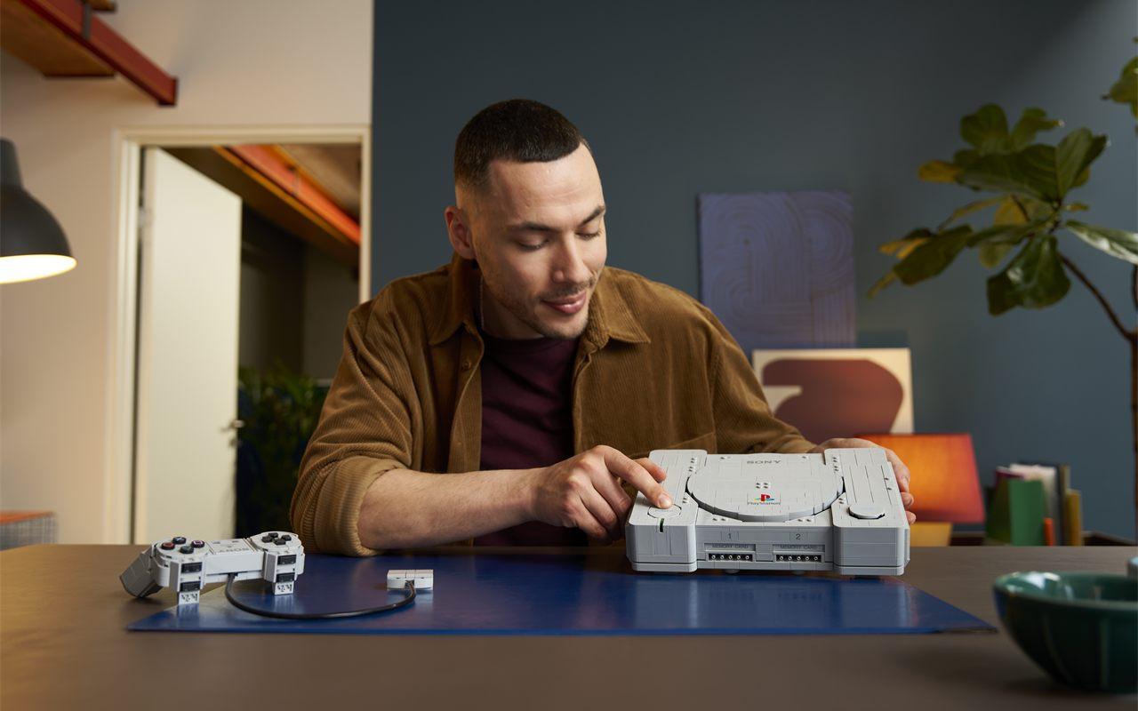 Un constructeur adulte appuie sur le bouton POWER de la PlayStation en briques