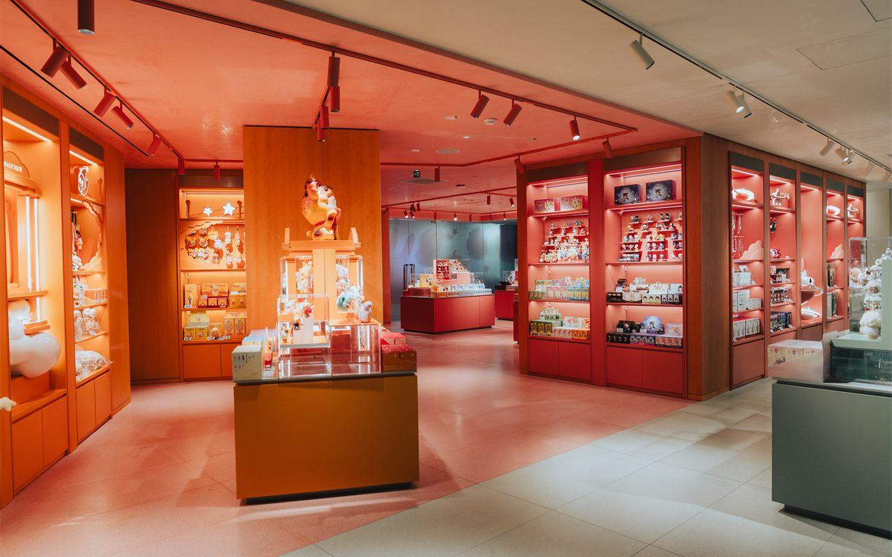 Étage du POP MART Haussmann baigné de lumière corail, meubles laqués rouge et vitrines éclairées