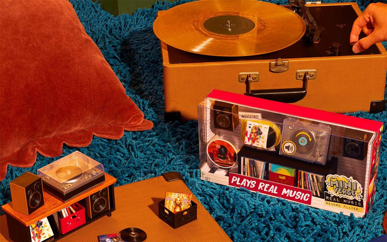 La mini platine Miniverse Real Music posée sur une valise-platine, à côté d'un vrai vinyle doré