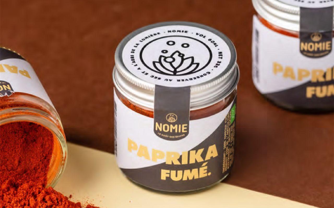 Pot de paprika fumé Nomie et poudre rouge renversée sur fond terracotta