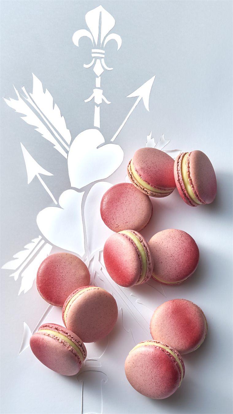 Macarons Ispahan posés sur un décor de papier découpé reprenant la fleur de lys et les flèches
