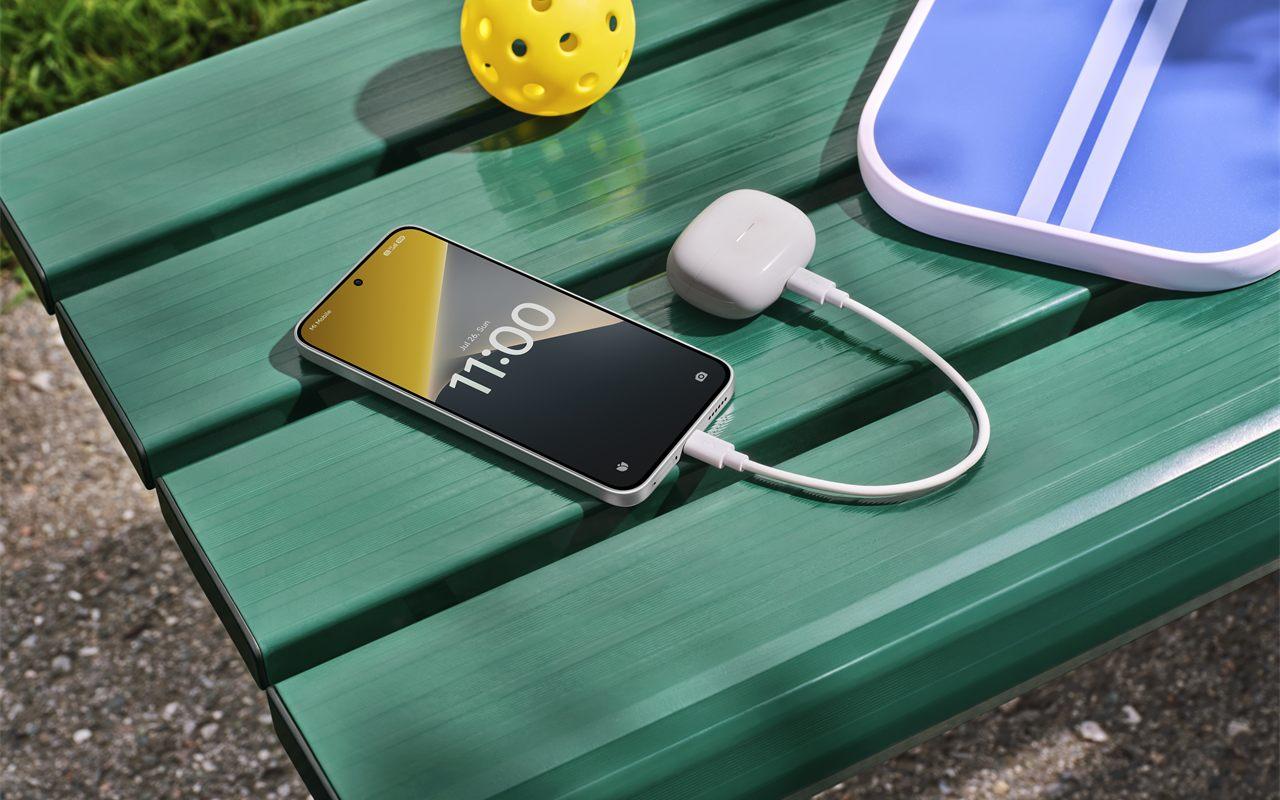 Le POCO X8 posé sur un banc recharge un boîtier d'écouteurs par câble
