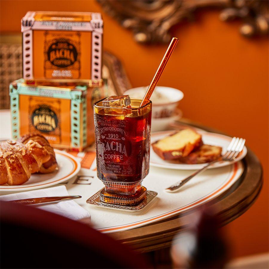 Café glacé Bacha Coffee servi avec une paille en verre, un croissant et une part de cake