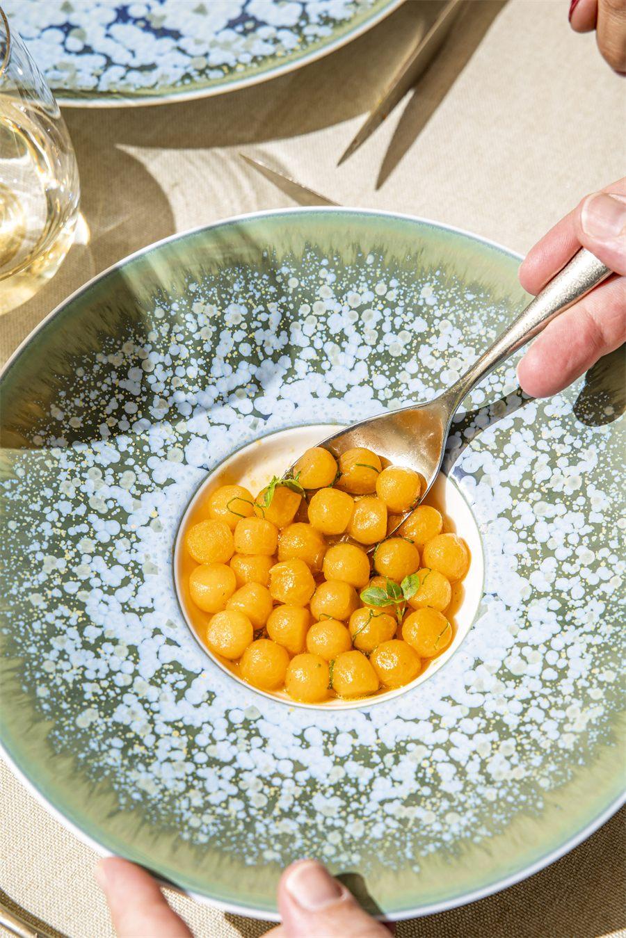 Petites billes orange nappées de sauce et parsemées d'herbes fraîches, au creux d'une grande assiette bleu et vert moucheté