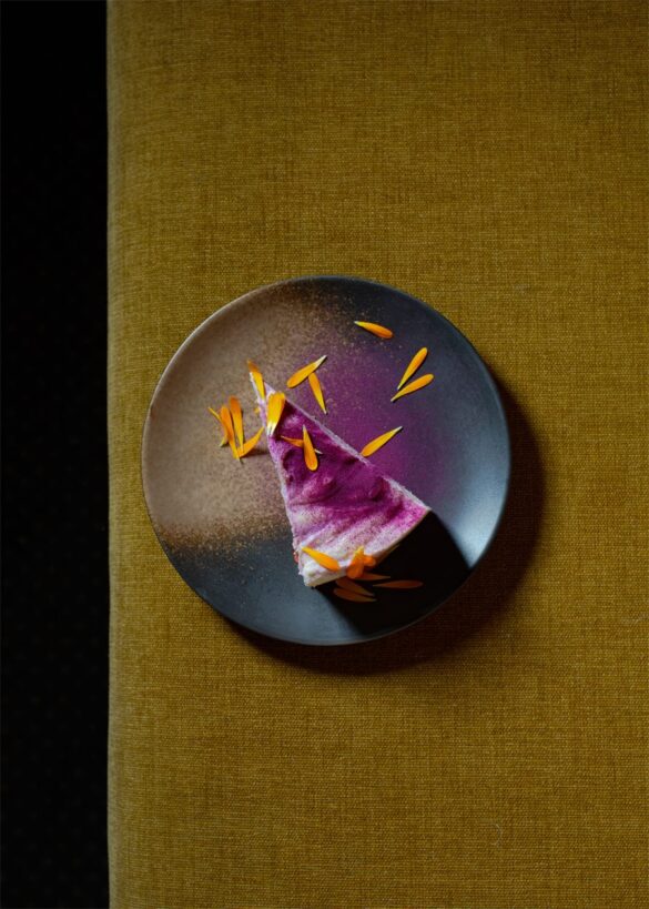 restaurant-sobo-cheesecake-ube-nomadeurbain Part de cheesecake a l'ube parsemee de petales orange, servie sur une assiette sombre chez SOBO