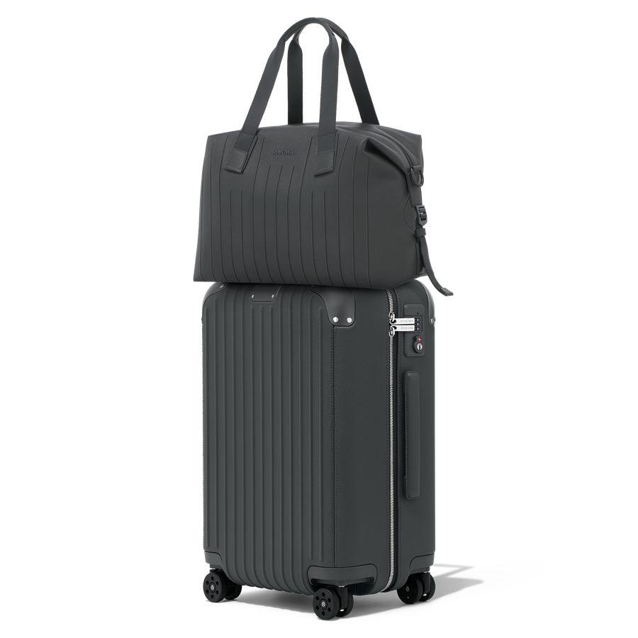 Sac de voyage Medium Never Still en cuir Anthracite pose sur la valise RIMOWA Distinct Cabin de meme teinte