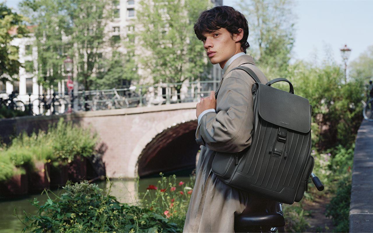 Grand sac a dos a rabat RIMOWA Never Still en cuir Anthracite porte le long d un canal d Amsterdam