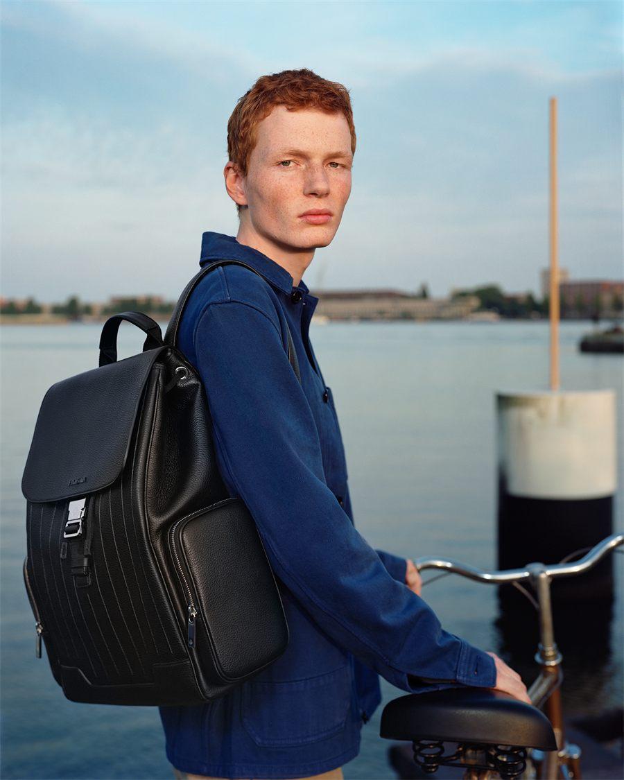 Grand sac a dos a rabat RIMOWA Never Still en cuir noir porte sur un quai d Amsterdam