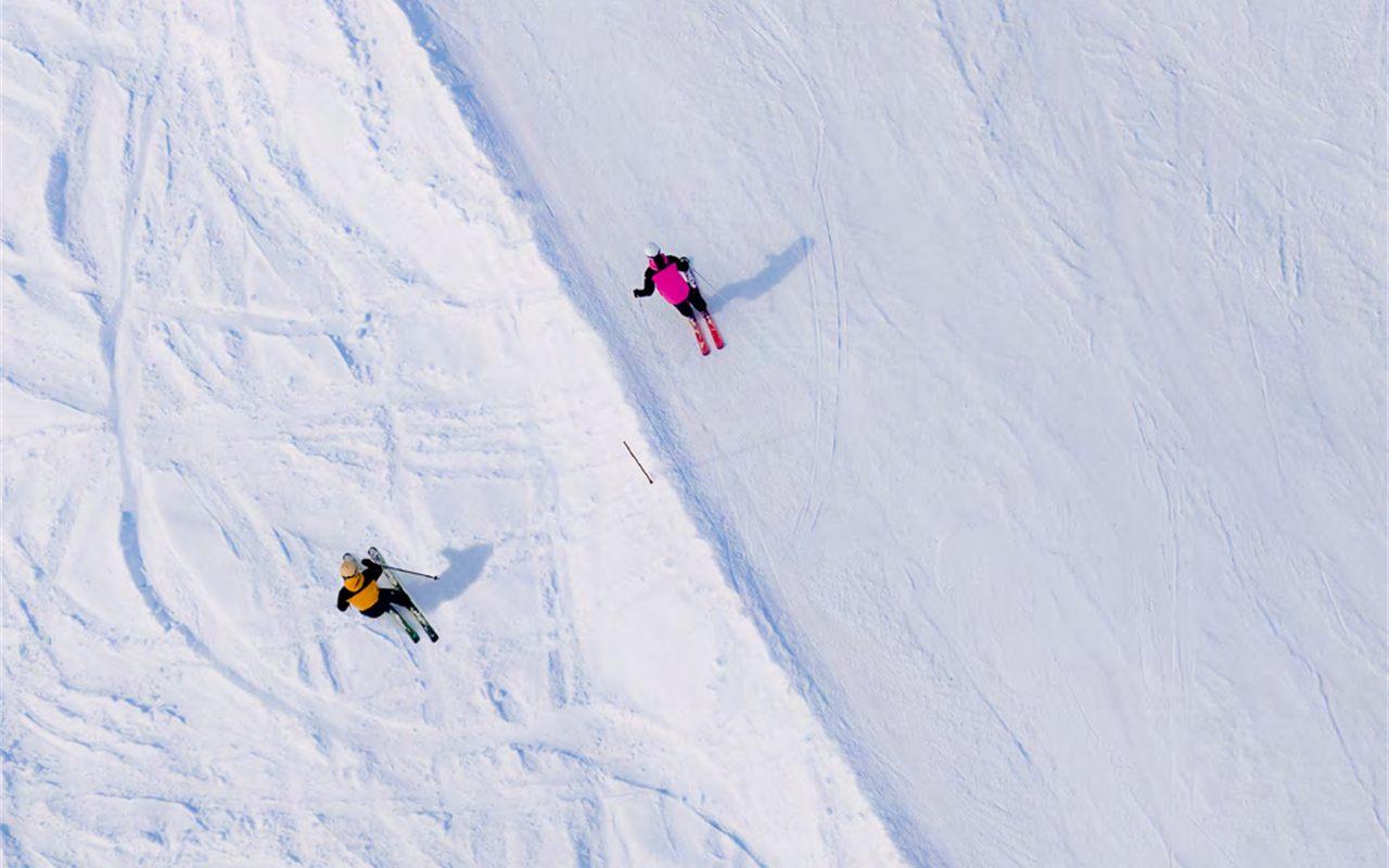 Vue aérienne d'une skieuse sur la piste damée et d'un skieur dans la neige tracée du bord de piste