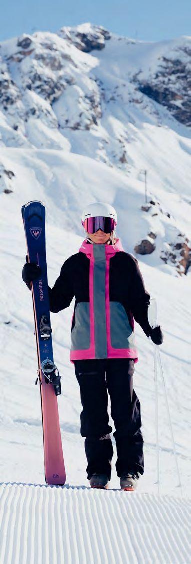 Skieuse en veste de ski Rossignol Outerlimits rose, bleu-vert et noir, skis à la main