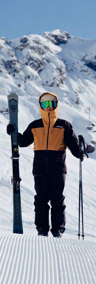 Skieur en veste de ski Rossignol Outerlimits moutarde et noir, skis à la main