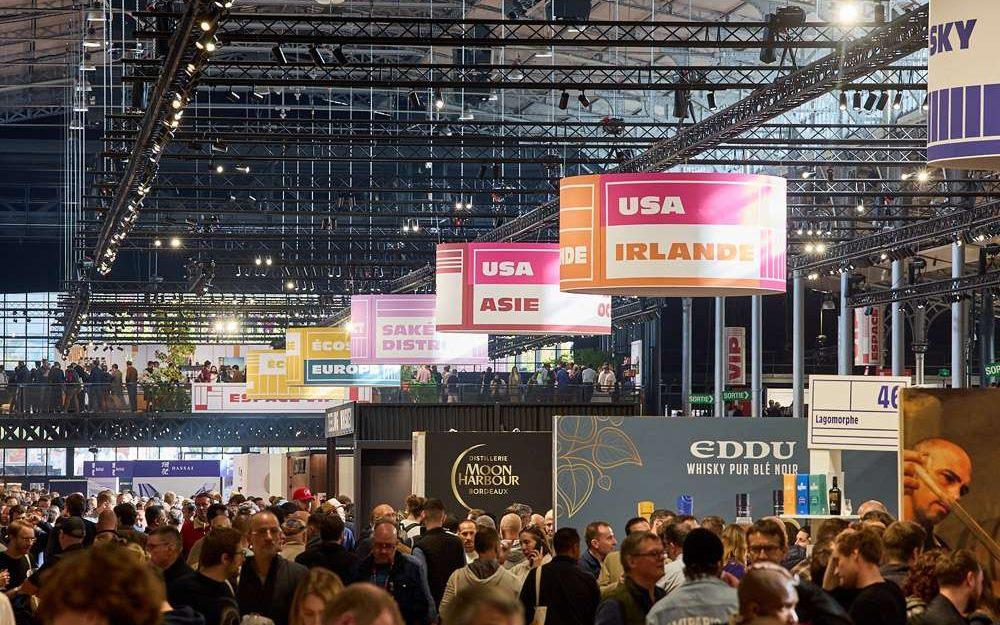 Foule et enseignes des pays exposants sous la charpente de la Grande Halle de la Villette au Whisky Live Paris
