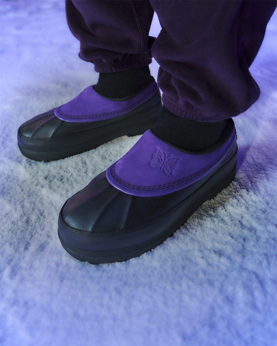 Sabot Ambler SOREL x NEEDLES porté dans la neige, nubuck violet sur caoutchouc noir