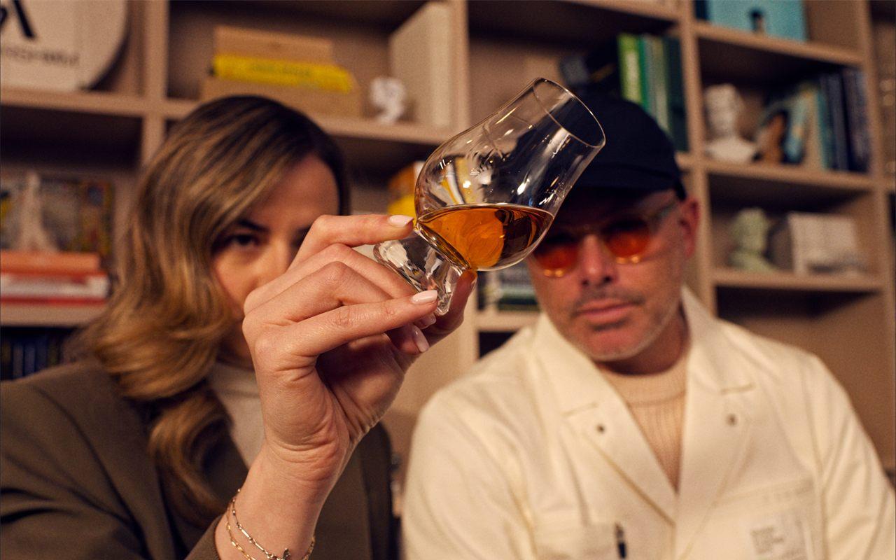 Un verre de dégustation The Balvenie tenu en lumière devant Daniel Arsham