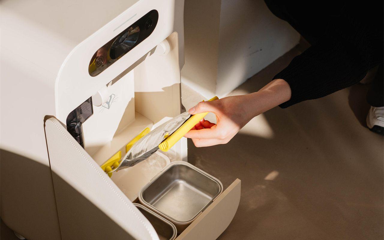 Une main glisse une recharge de pâtée dans le distributeur YOMY