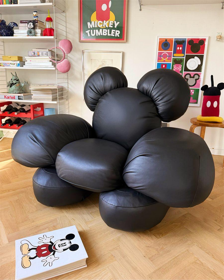 Le fauteuil Mickey en cuir noir dans un salon décoré d'affiches Mickey