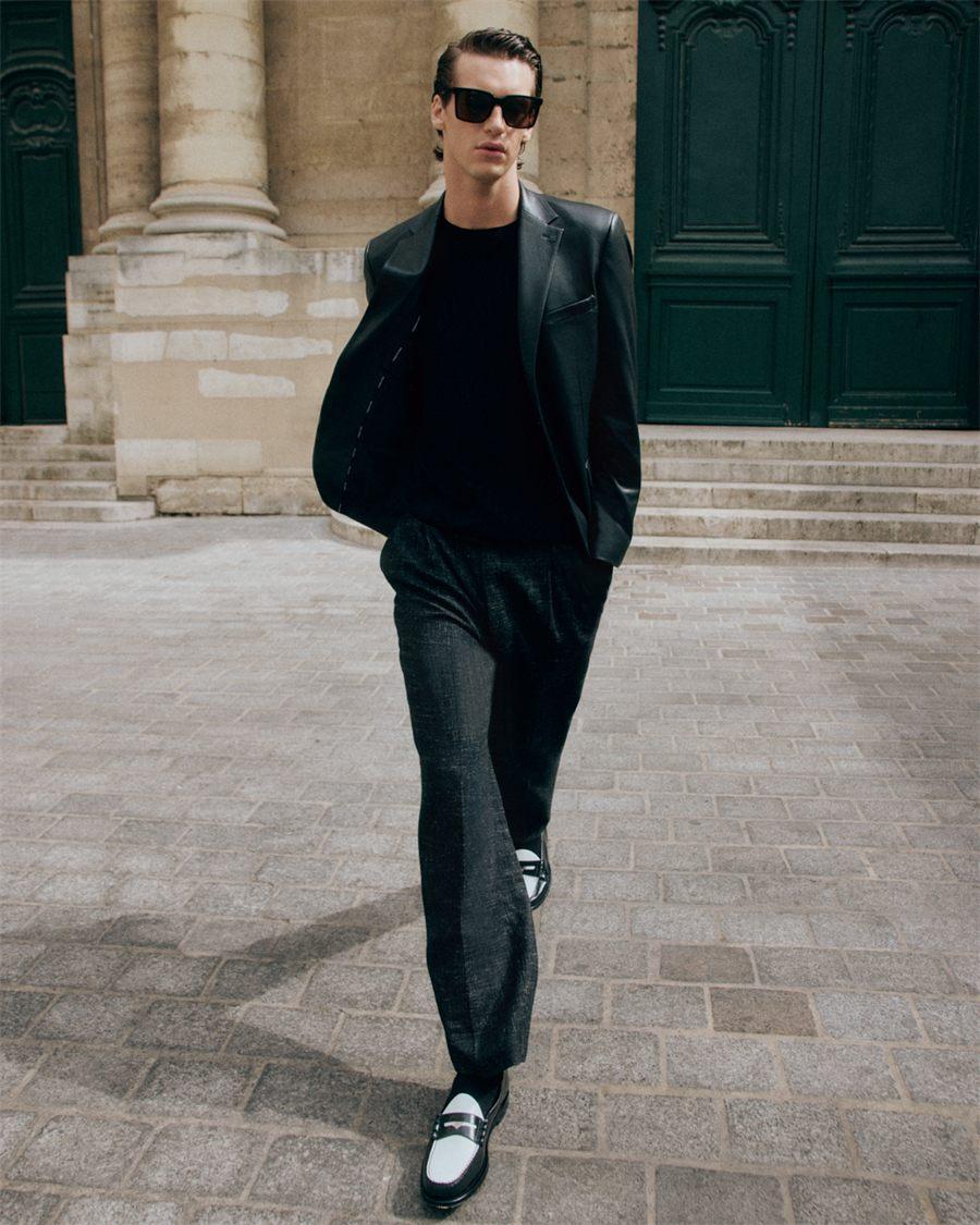 Homme en tenue noire chaussé de mocassins penny noir et blanc