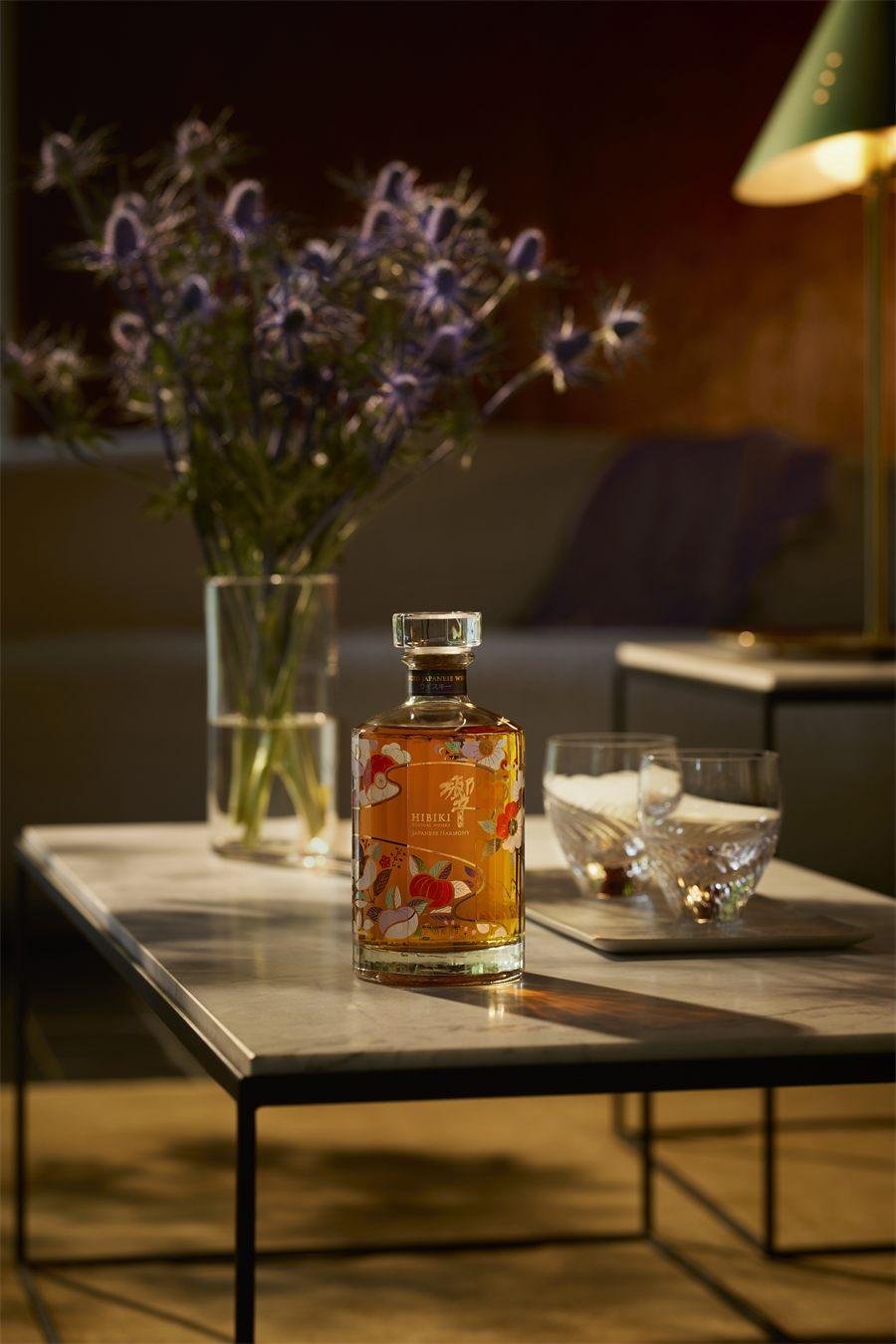 Flacon Hibiki Japanese Harmony Chiso sur une table basse en marbre, près d'un plateau de verres à whisky