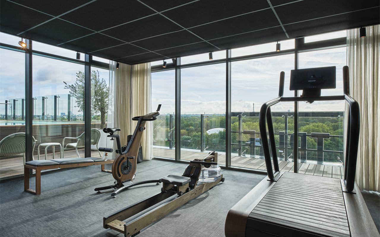 Salle de sport vitrée de l'hôtel avec rameur en bois, face au bois de Boulogne